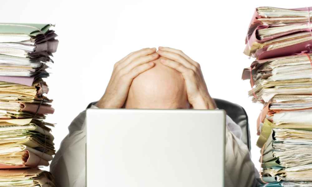 guy with hands on head between stacks of paper