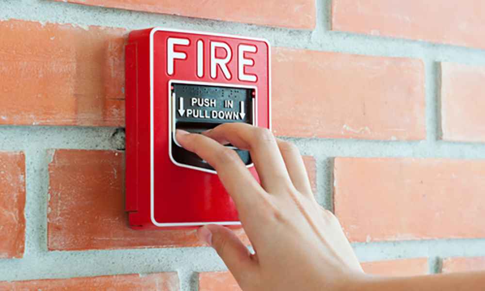 hand touching fire alarm on brick wall